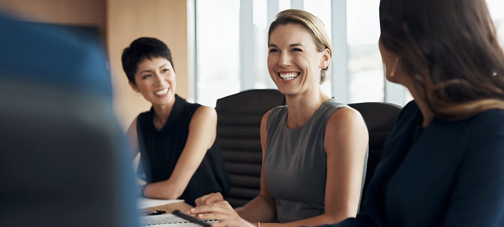 Trois femmes souriantes à une table de conférence