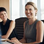 Trois femmes souriantes à une table de conférence