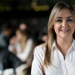 Photo d'une femme souriante debout à une terrasse où sont attablées des personnes