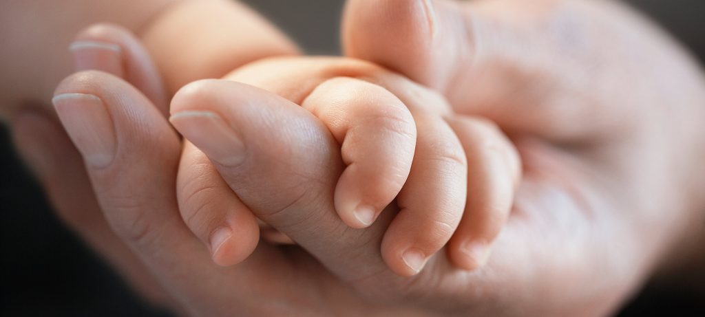 Gros plan sur une main adulte qui tient la main d'un bébé
