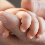 Gros plan sur une main adulte qui tient la main d'un bébé