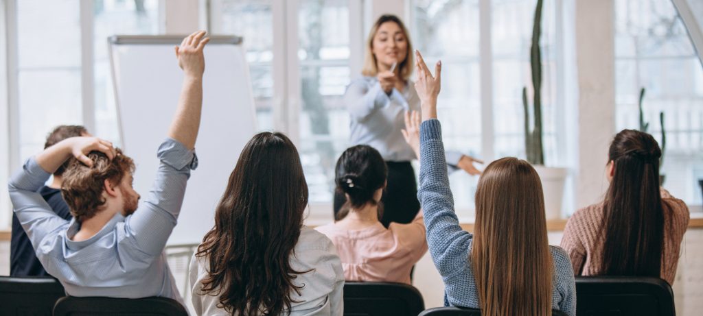 Une enseignante face à une classe d'adultes avec la main levée