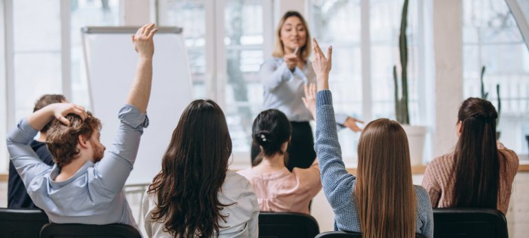 Une enseignante face à une classe d'adultes avec la main levée