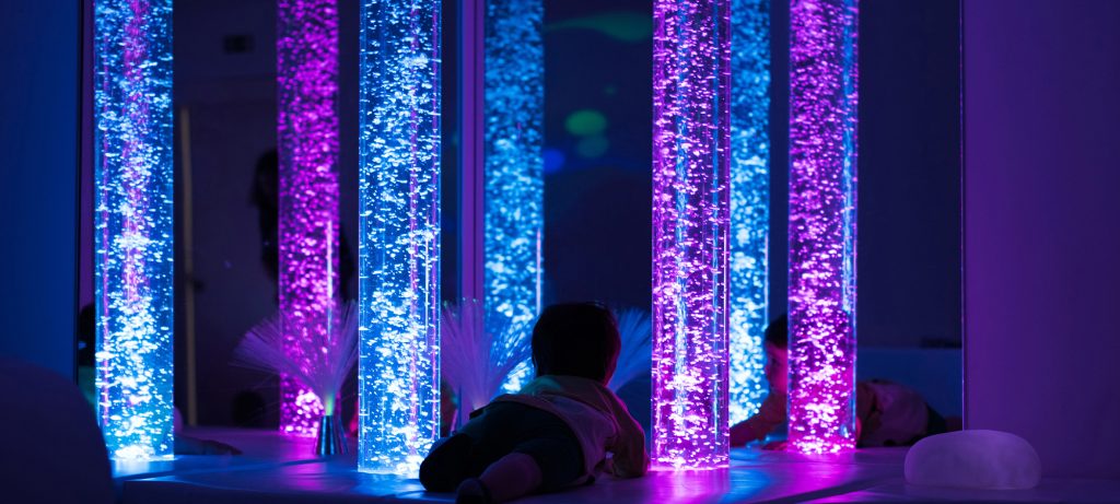 Un enfant à plat ventre regarde des tubes à bulles dans une salle multisensorielle