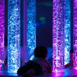 Un enfant à plat ventre regarde des tubes à bulles dans une salle multisensorielle