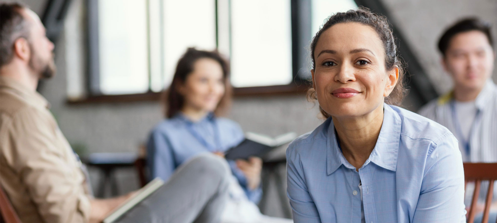 Personne assise sur une chaise regardant la caméra avec une équipe discutant en arrière